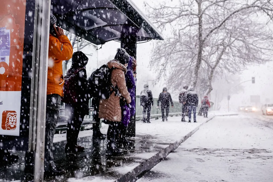 Crowded bus stop in a snowy winter day, people waiting as snow falls heavily.