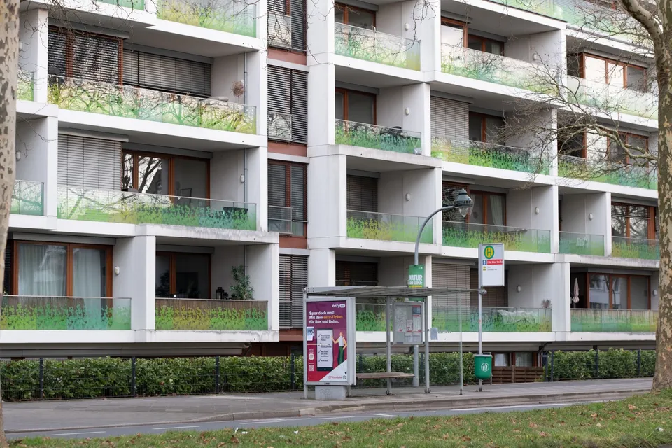 A modern urban apartment with balconies and a nearby bus stop in a city setting.
