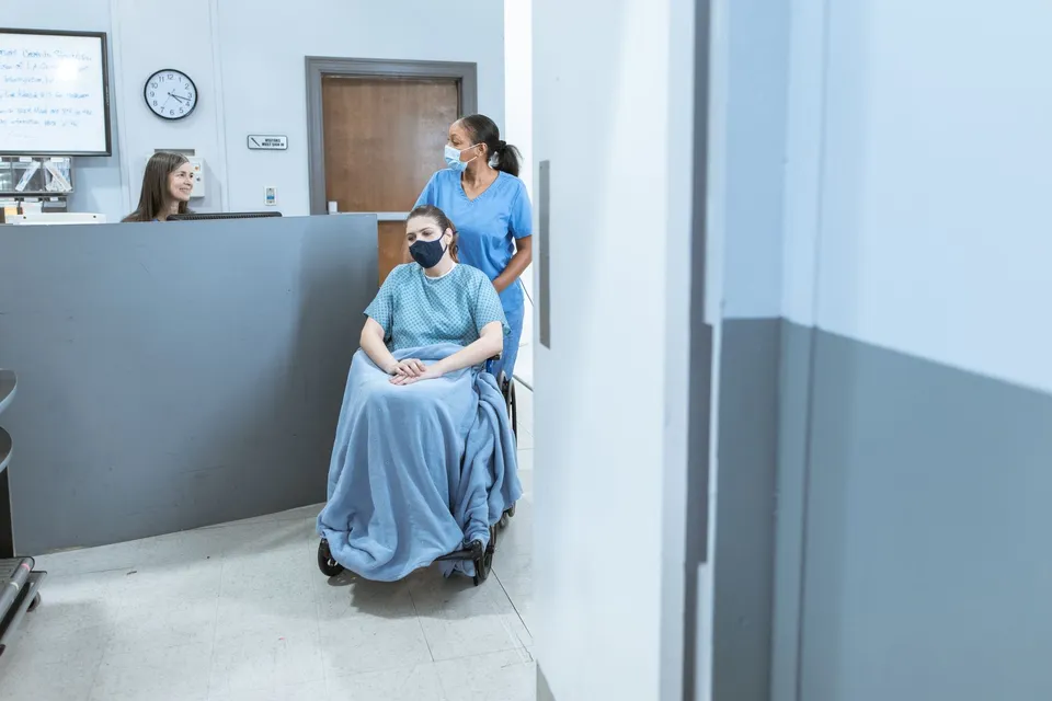 Nurse assisting a patient in a wheelchair at a medical facility reception.