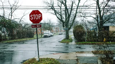 A quiet residential street in winter, featuring a prominent stop sign amidst falling snow.