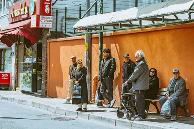 A diverse group of people waiting at a bus stop in an urban setting during the day.